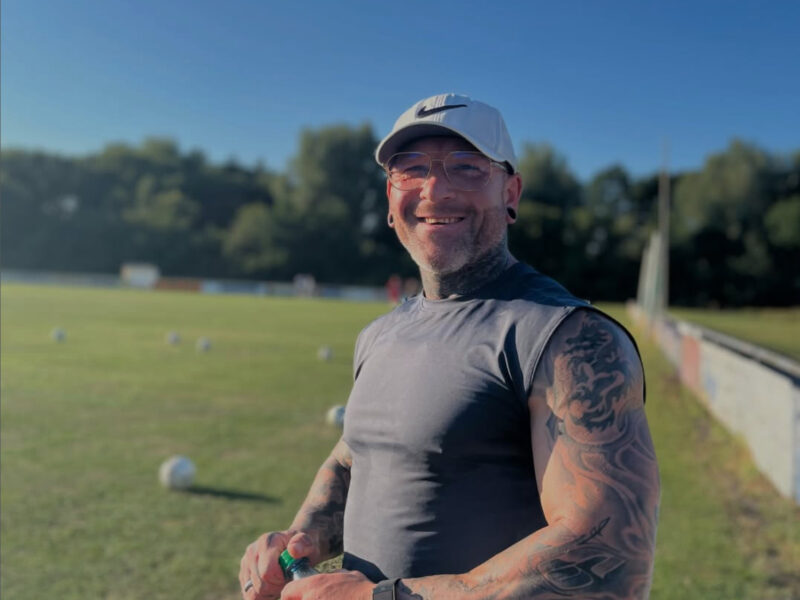 Tim Amberger – ein Fitnesscoach, Ernährungsberater und Trainer draußen im Sommer auf einem Sportplatz